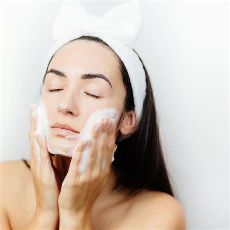 Donna che si deterge il viso con un prodotto schiumogeno
