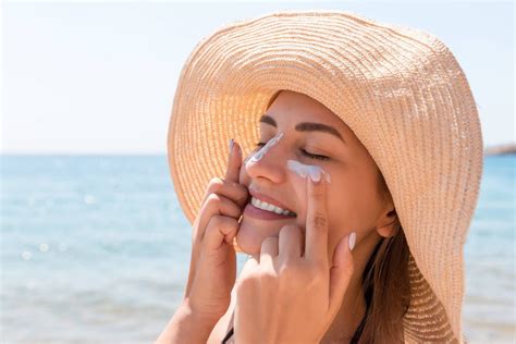 Donna che applica crema solare sul viso con un sorriso