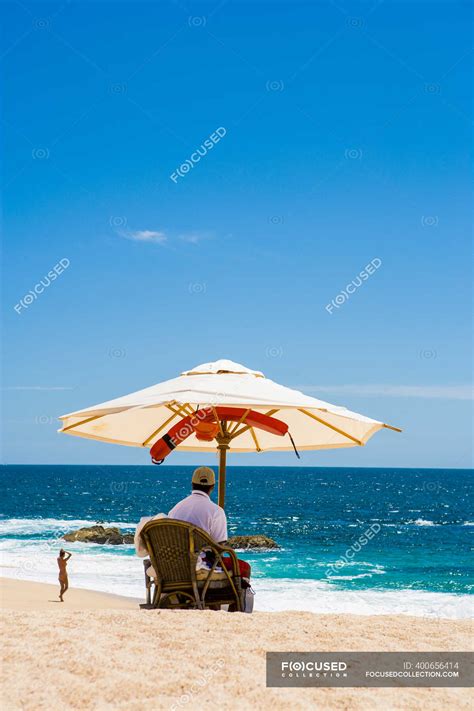Immagine di una spiaggia tranquilla con un ombrellone e una persona che legge un libro